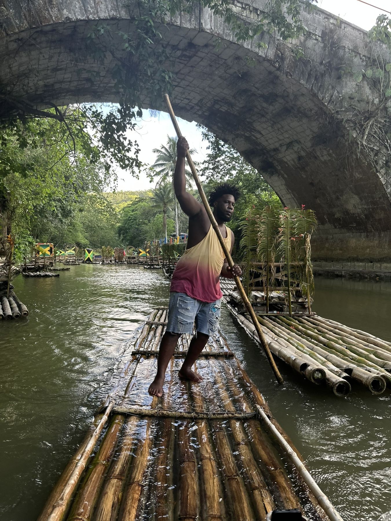 Raft captain poling a bamboo raft under a stone bridge on the Great River, Lethe