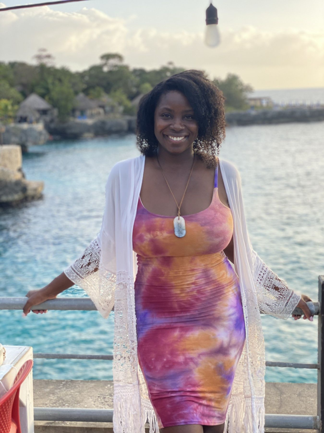 Nikki at a cliff rail above a turquoise cove in Negril at golden hour