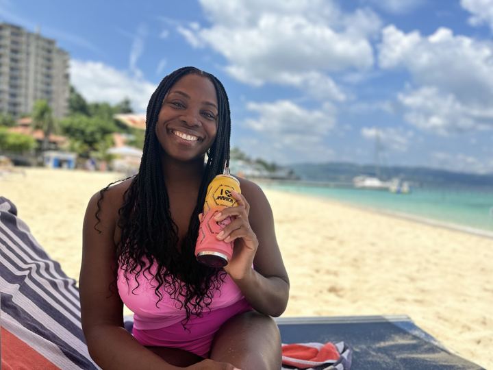 Nikki raising a drink on a lounger at Doctor's Cave Beach with the bay behind